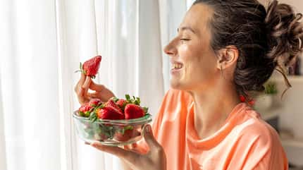 Eine Frau hält lächelnd eine Schale mit Erdbeeren