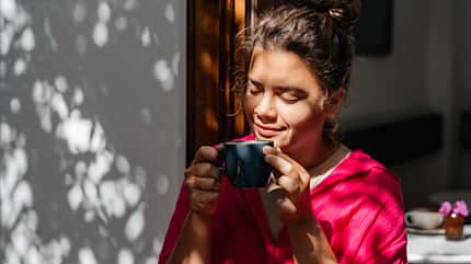 Junge Frau in pinkem Sweatshirt genießt ihren Kaffee in der Sonne