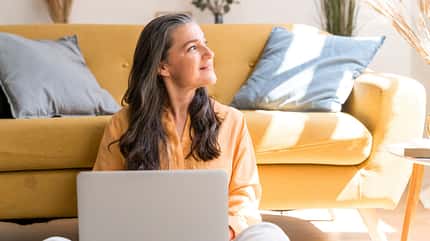 Eine ältere Dame sitzt am Laptop und schaut aus dem Fenster Eine ältere Dame sitzt am Laptop und schaut aus dem Fenster