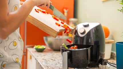 Eine weibliche Hand, die Gemüse von einem Schneidebrett in den Airfryer füllt