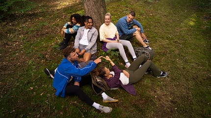 Mehrere junge Menschen sitzen im Freien unter einem Baum Mehrere junge Menschen sitzen im Freien unter einem Baum
