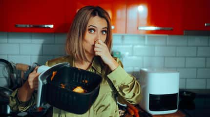Eine Frau die einen dreckigen Airfryer-Korb in der Hand hält und sich die Nase zuhält Eine Frau die einen dreckigen Airfryer-Korb in der Hand hält und sich die Nase zuhält