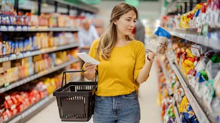 Eine Frau im Supermarkt checkt die Zutatenliste von einem Fertigprodukt Eine Frau im Supermarkt checkt die Zutatenliste von einem Fertigprodukt
