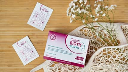 OMNi-BiOTiC® WOMAN Packung auf einem Tisch mit Einkaufsbeutel und Blumen OMNi-BiOTiC® WOMAN Packung auf einem Tisch mit Einkaufsbeutel und Blumen