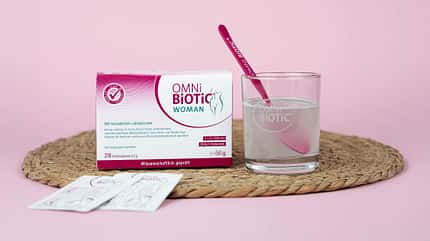 Packung OMNi-BiOTiC® WOMAN und ein Glas mit Löffel und aufgelöstem Pulver Packung OMNi-BiOTiC® WOMAN und ein Glas mit Löffel und aufgelöstem Pulver
