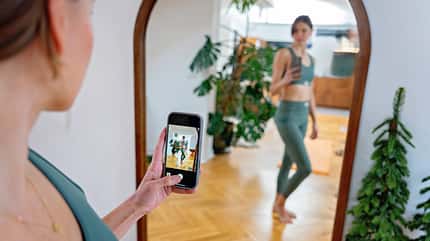 Eine junge Frau in Sportkleidung fotografiert sich selbst im Spiegel Eine junge Frau in Sportkleidung fotografiert sich selbst im Spiegel
