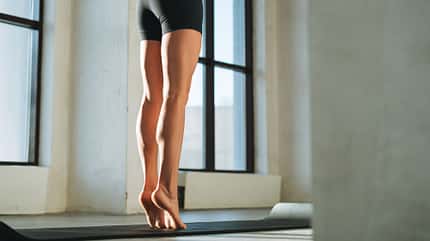 Eine junge Frau steht barfuß auf Zehenspitzen auf einer Yogamatte. Eine junge Frau steht barfuß auf Zehenspitzen auf einer Yogamatte.