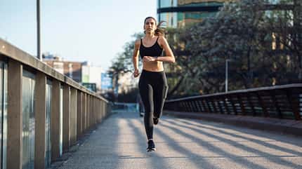 Eine Frau joggt über eine Brücke in einer städtischen Umgebung.