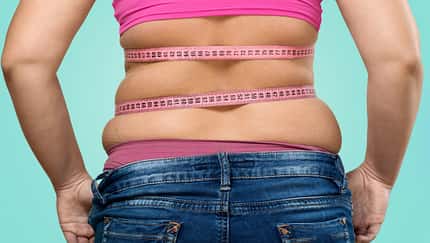 Frau mit sichtbarem Bauchspeck über der Hose wird von hinten mit einem Maßband über dem bauch gezeigt.