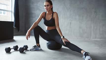 Frau stretcht ihr Bein und hat Hanteln und einen Fitnessball dabei
