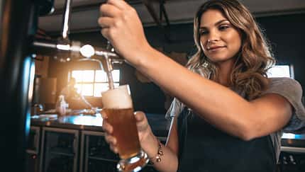 Young,Woman,Dispensing,Beer,In,A,Bar,From,Metal,Spigots.