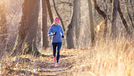 Joggerin läuft in langem Sportoutfit durch einen herbstlichen Wald