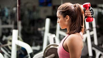 Frau im Gym macht Trizeps-Übung mit Hantel