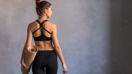Frau mit einer Yogamatte unter dem Arm ist in der Rückenansicht zu sehen