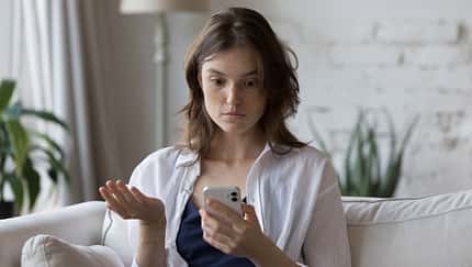 Junge Frau schaut schockiert auf ihr Smartphone-Display