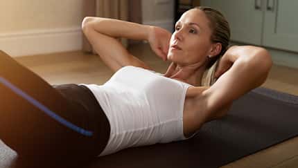 Frau um die 40 macht Crunches zu Hause auf der Fitnessmatte