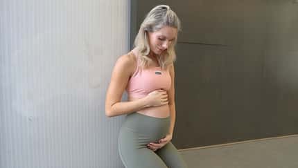 Kaya Renz schaut in Sportkleidung auf ihren Babybauch und berührt diesen