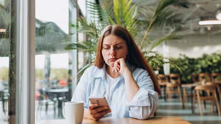Frau sitzt mit Handy in einem Café und sieht traurig aus