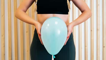 Frau hält sich aufgepusteten Luftballon vor den Bauch.