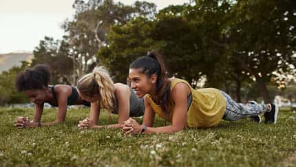 Drei Frauen machen Planks im Park.