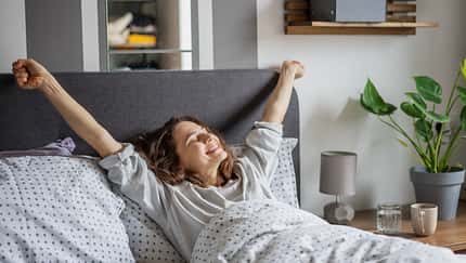 Young,Smiling,Woman,Waking,Up,Lying,In,Bed,Stretching,With