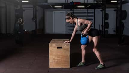 Durchtrainierte Frau rudert mit einer Kettlebell.