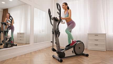 Woman,With,Towel,Using,Modern,Elliptical,Machine,At,Home