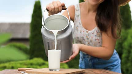 junge Frau kippt frische Milch in ein Glas