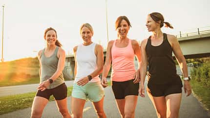 vier fröhliche und fitte Frauen gehen in Sportkleidung einen Weg entlang