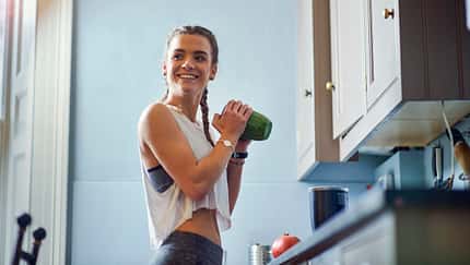 Young woman shaking juicer at kitchen counter