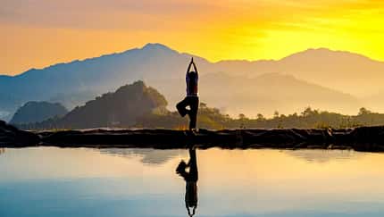 Eine Frau stretcht sich mithilfe einer Yoga-Pose vor den Bergen