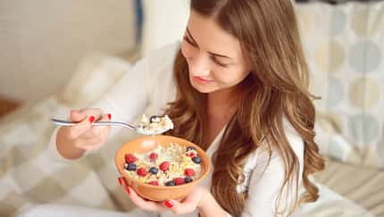 Frau im Schlafanzug isst Müsli mit Beeren