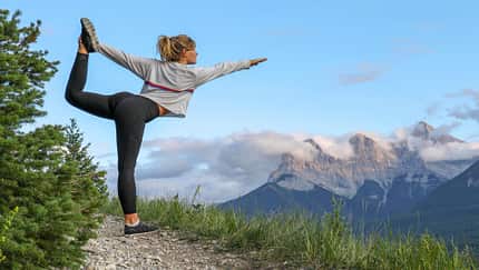 Junge Frau macht eine Yoga-Pose auf einem Bergweg