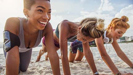 Three young women doing push-ups on the beach