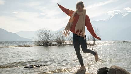 Frau hüpft von Stein zu Stein am See