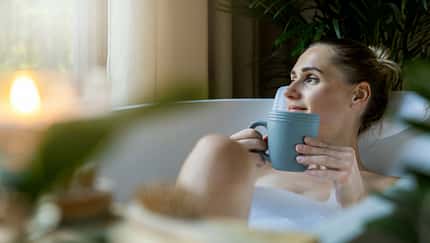 woman relaxing in bath and drink a coffee at home bathroom. looking out of window
