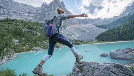 Frau springt über Steine in Berglandschaft