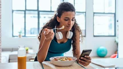 Junge Frau isst einen Salat und schaut auf ihr Handy