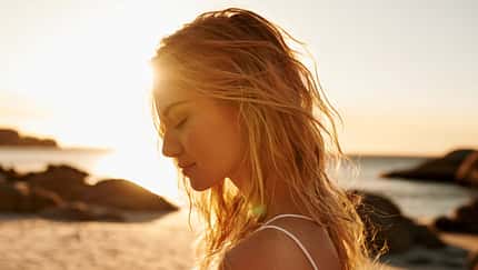 Eine Frau mit blonden Haaren am Strand bei Sonnenuntergang