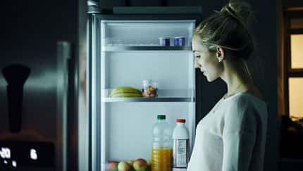 Eine Frau steht nachts vor dem Kühlschrank und schaut, was sie essen möchte