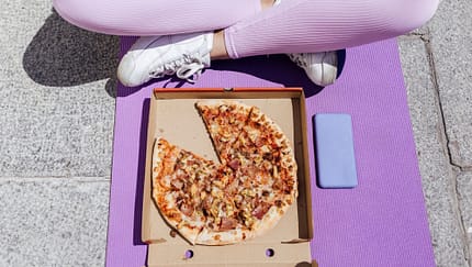 Eine Frau sitzt im Schneidersitz und isst Pizza