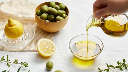 Eine Glaskanne mit Olivenöl, Oliven und Zitronen im Hintergrund Eine Glaskanne mit Olivenöl, Oliven und Zitronen im Hintergrund