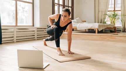 Eine Frau praktiziert Yoga auf einer Matte vor einem Laptop