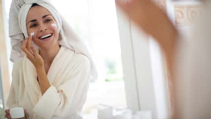 Eine Frau im Bademantel mit Turban cremt sich ihr Gesicht ein Eine Frau im Bademantel mit Turban cremt sich ihr Gesicht ein