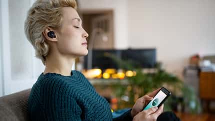 Eine Frau mit geschlossenen Augen die ein Smartphone in der Hand hält Eine Frau mit geschlossenen Augen die ein Smartphone in der Hand hält