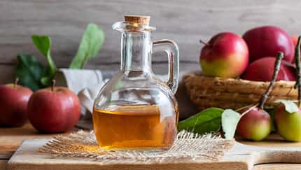 Karaffe mit Apfelessig und Äpfeln im Hintergrund Karaffe mit Apfelessig und Äpfeln im Hintergrund