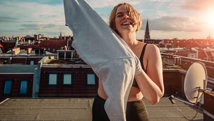 aspiration,body positivity,confident,delight,millennials,urban,wanderlust Portrait of smiling woman wearing t-shirt on rooftop against dramatic sky