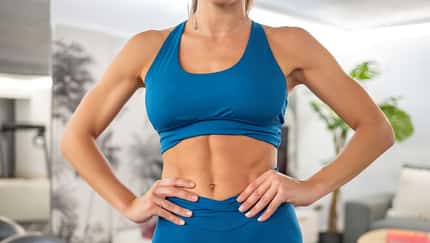 Eine trainierte Frau in blauer Sportkleidung zeigt ihre trainierten Bauchmuskeln