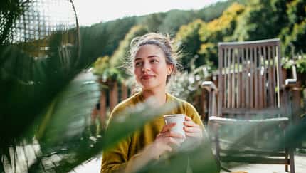 Woman with morning cup of coffee, sitting on patio and enjoying moment for herself. Portrait of beautiful woman.