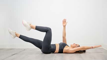 Woman performing dead bug exercise lowering opposite arm and leg for functional core training